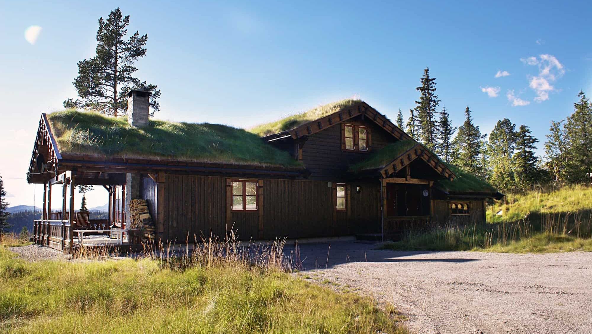 Tradisjonell hytte med torvtak, omgitt av natur og med utsikt i solfylt landskap.